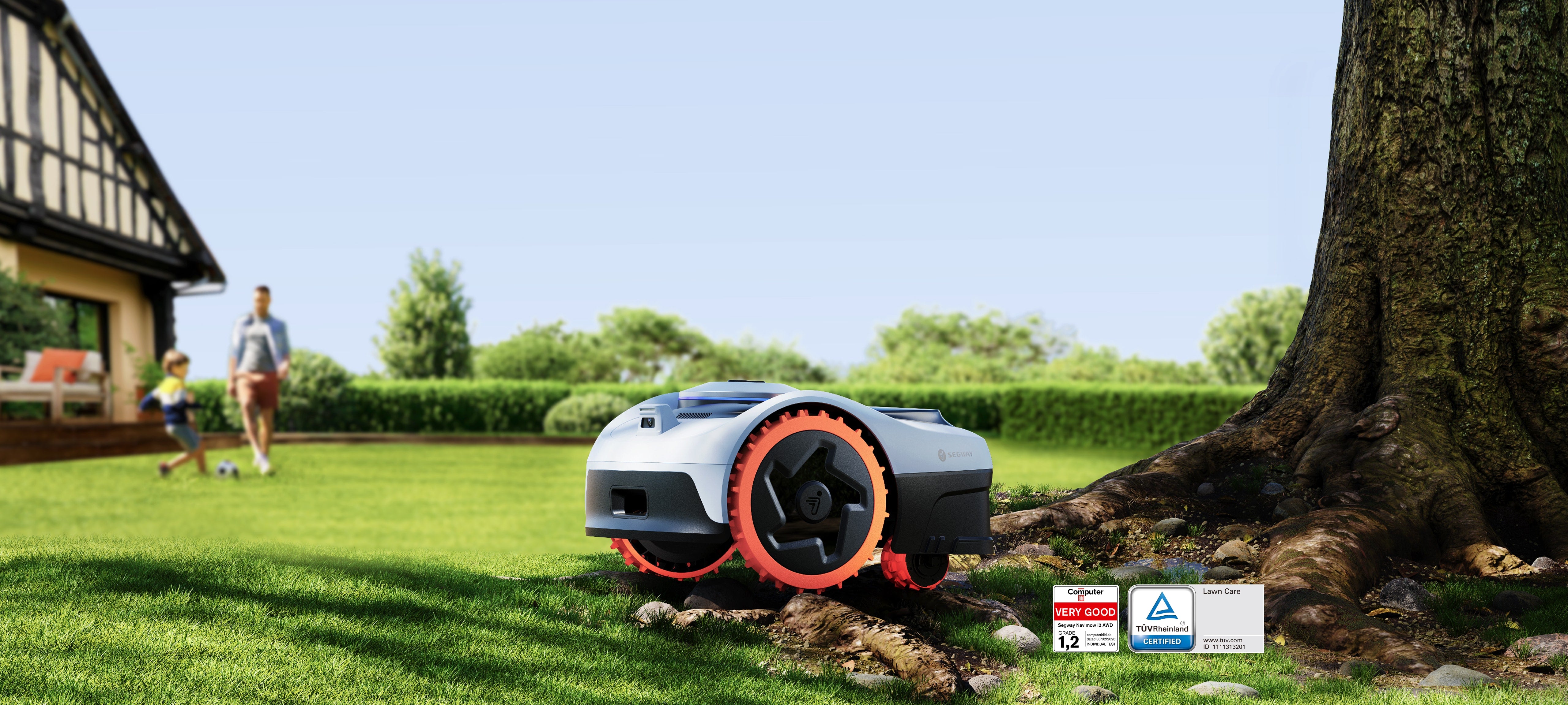 Navimow i2 AWD robot lawn mower on a lawn beside a large tree with a timber-framed house and people in soft focus