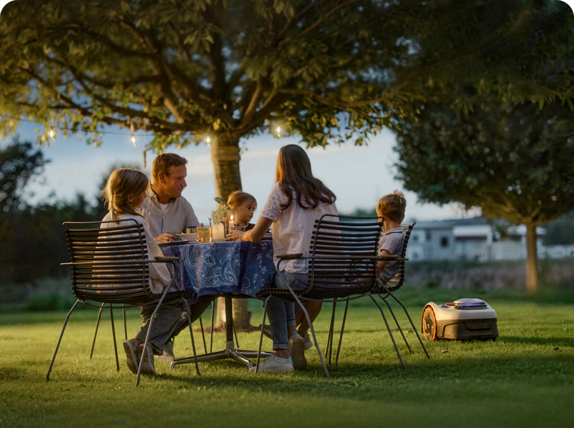 Family eating dinner with Navimow i110E robot lawn mower nearby.