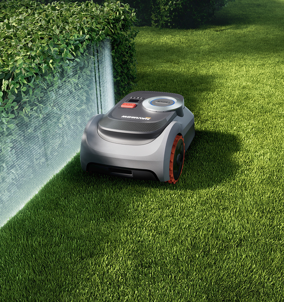 Navimow i105E robot lawn mower mows green grass near hedge.